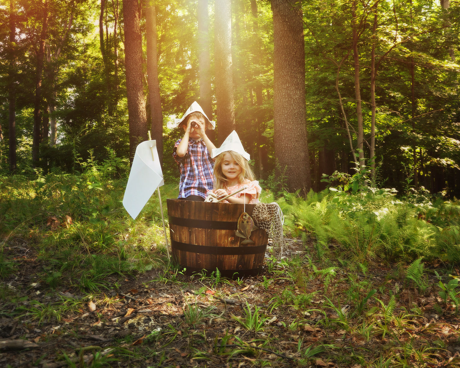Junge und Mädchen sitzen in Holzfass im Wald und spielen Schiff fahren